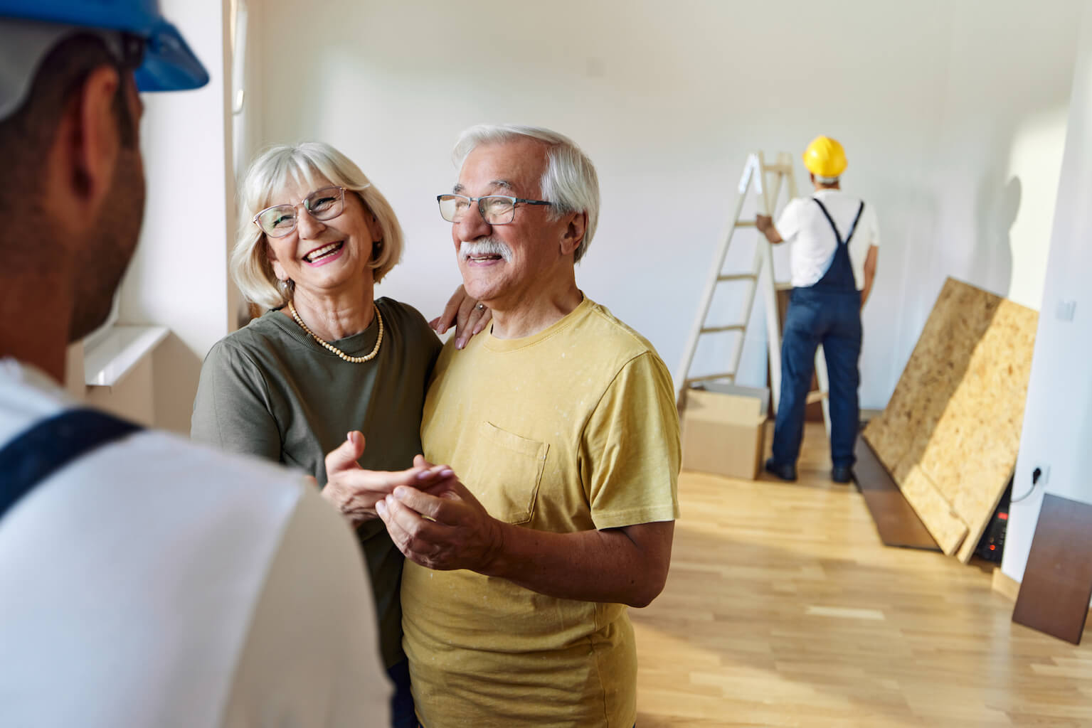 Senioren Ehepaar spricht mit Bauleiter, im Hintergrund ein Bauarbeiter 