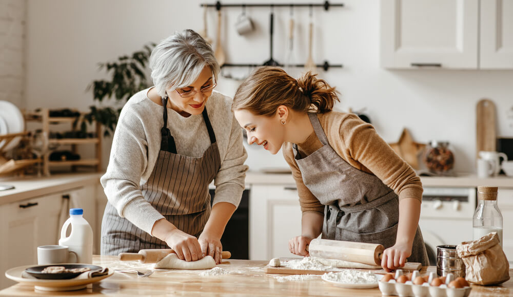 Glückliche Seniorin und Haushaltshilfe backen gemeinsam