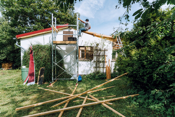 Mann auf einem Baugerüst nimmt Renovierungsarbeiten an einem Haus vor 