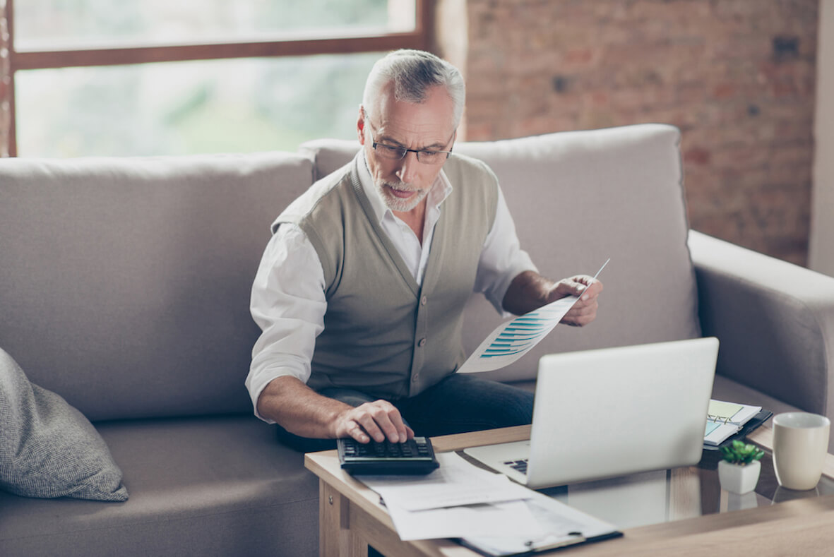 Senior sitzt auf dem Sofa und führt Berechnungen am Laptop durch