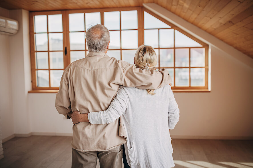 Ehepaar von hinten steht Arm in Arm in einer leeren Wohnung